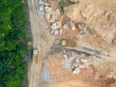 Aerial view of a mining site with dump trucks transporting earth and rocks surrounded by dense forest in Bukit Tambun Penang Malaysia. Aerial view of a mining site with dump trucks transporting earth and rocks surrounded by dense forest in Bukit Tambun Penang Malaysia.