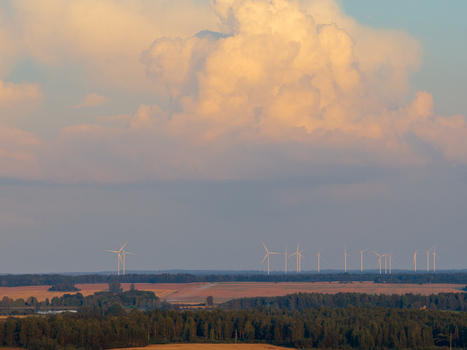 Aerial view of wind turbines standing across a rural landscape with agricultural fields and forests under massive cumulus clouds at sunset Taujenai Vilnius County Lithuania.