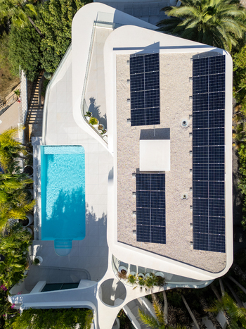 Aerial view of a modern white villa featuring a turquoise swimming pool and solar panels on the roof surrounded by lush greenery in Moraira Valencian Community Spain.