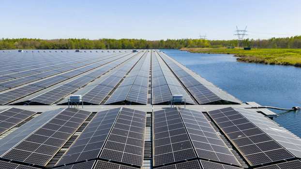 Aerial view of rows of floating solar panels on a calm lake surrounded by green trees and power lines under a clear blue sky in Zwolle Overijssel Netherlands. Aerial view of rows of floating solar panels on a calm lake surrounded by green trees and power lines under a clear blue sky in Zwolle Overijssel Netherlands.