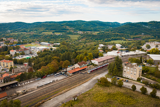 Aerial view of a train station with a passenger train stopped at the platform surrounded by lush green hills and buildings in Buzet Istria County Croatia.