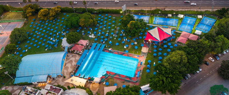 Aerial view of a swimming pool complex with blue umbrellas on the lawn sports courts and lush trees in Tel Aviv Yafo Tel Aviv District Israel. Aerial view of a swimming pool complex with blue umbrellas on the lawn sports courts and lush trees in Tel Aviv Yafo Tel Aviv District Israel.