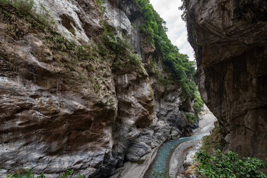 View of Taroko National Park featuring steep marble canyon walls a turquoise river flowing through the gorge and lush vegetation on the cliffs in Xiulin Township Hualien County Taiwan.