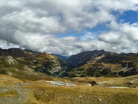 Aerial view of Grossglockner High Alpine Road with a person in a yellow jacket standing on a rocky outcrop amidst mountain peaks and valleys in Zell am See District Salzburg Austria.