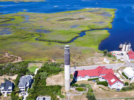 Aerial view of Oak Island Lighthouse surrounded by coastal wetlands marshlands and nearby residential buildings in Caswell Beach North Carolina United States.