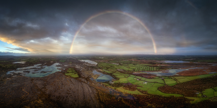 Aerial view of a vibrant full rainbow arching over the limestone pavement and green fields of the Burren under dramatic storm clouds in Burren County Clare Ireland.