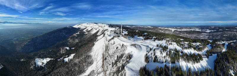Aerial view of snow capped mountains a radio tower piercing the sky and a winding ski slope carving through the frosted landscape Gex Auvergne Rhône Alpes France. Aerial view of snow capped mountains a radio tower piercing the sky and a winding ski slope carving through the frosted landscape Gex Auvergne Rhône Alpes France.