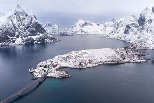 Aerial view of Lofoten featuring snow covered mountains a bridge connecting islands and coastal settlements in Nordland Norway.