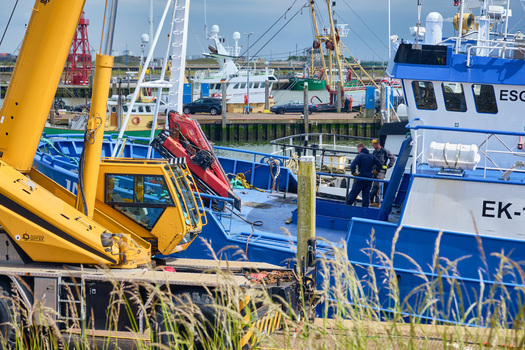 Den Oever Netherlands 18 May 2026 View of British fleet vessels being renovated at the Machinefabriek fishing repair wharf with a large yellow crane and workers in the harbor.