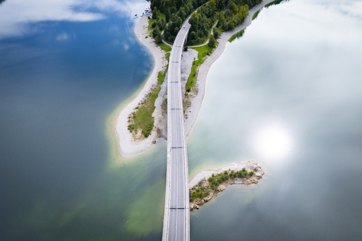 Aerial view of a bridge cutting through the blue waters of Sylvensteinspeicher Lake surrounded by verdant forests Lenggries Bavaria Germany. Aerial view of a bridge cutting through the blue waters of Sylvensteinspeicher Lake surrounded by verdant forests Lenggries Bavaria Germany.