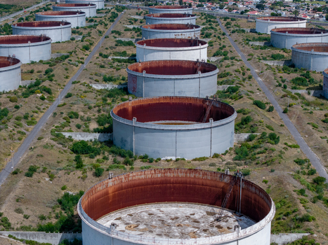 Aerial view of industrial oil storage tanks in Milnerton featuring large circular steel containers with rusty interiors surrounded by dry vegetation in Cape Town Western Cape South Africa. Aerial view of industrial oil storage tanks in Milnerton featuring large circular steel containers with rusty interiors surrounded by dry vegetation in Cape Town Western Cape South Africa.