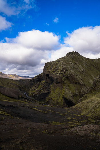 View of a dramatic landscape with a rugged mountain cloaked in green moss and dark volcanic soil under a bright blue sky Skaftárhreppur Iceland. View of a dramatic landscape with a rugged mountain cloaked in green moss and dark volcanic soil under a bright blue sky Skaftárhreppur Iceland.