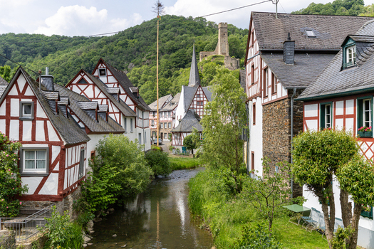 View of historic half timbered houses along a narrow river with a castle ruin on a green hill under a bright sky Monreal Rhineland Palatinate Germany. View of historic half timbered houses along a narrow river with a castle ruin on a green hill under a bright sky Monreal Rhineland Palatinate Germany.