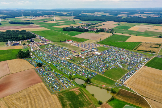 Herzogenaurach Germany 25 July 2025 Aerial view of the Open Beatz Festival campsite with colorful tents spread across green fields surrounded by forests and wind turbines. Herzogenaurach Germany 25 July 2025 Aerial view of the Open Beatz Festival campsite with colorful tents spread across green fields surrounded by forests and wind turbines.