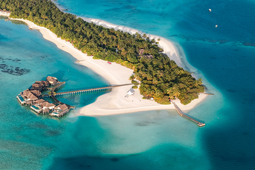 Aerial view of a tropical island resort with overwater bungalows a wooden jetty white sandy beaches and lush palm trees near Kudahuvadhoo Dhaalu Atoll Maldives. Aerial view of a tropical island resort with overwater bungalows a wooden jetty white sandy beaches and lush palm trees near Kudahuvadhoo Dhaalu Atoll Maldives.