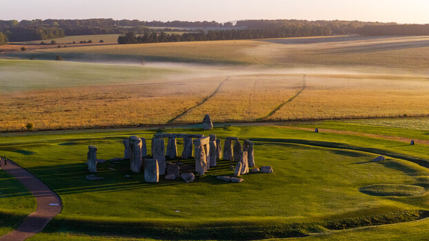 Aerial view of the prehistoric monument Stonehenge surrounded by lush green fields and morning mist in the English countryside near Salisbury England United Kingdom. Aerial view of the prehistoric monument Stonehenge surrounded by lush green fields and morning mist in the English countryside near Salisbury England United Kingdom.