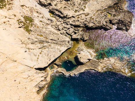 Aerial view of the Blue Hole at Dwejra Bay with people swimming in the natural pool surrounded by rugged limestone cliffs in Gozo Region Malta. Aerial view of the Blue Hole at Dwejra Bay with people swimming in the natural pool surrounded by rugged limestone cliffs in Gozo Region Malta.