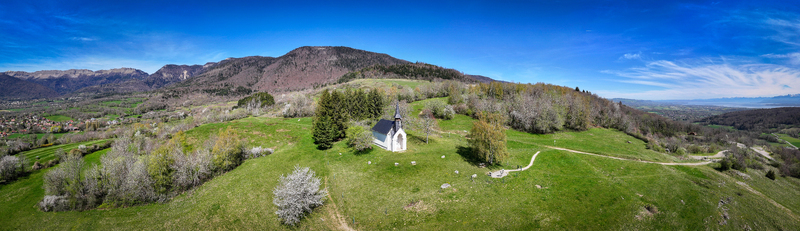 Aerial view of the Chapelle Notre Dame de Riantmont on a green hill with mountains in the background in Vesancy Auvergne Rhone Alpes France.