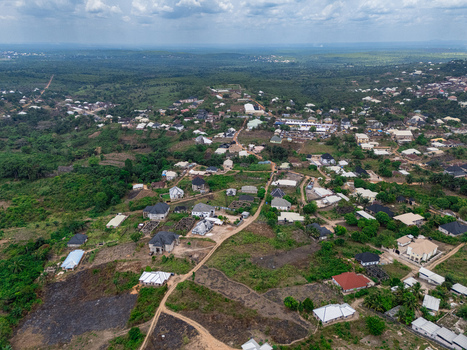 Aerial view of a residential area with scattered homes verdant trees reddish brown cleared land under a cloudy sky Ohafia Abia Nigeria. Aerial view of a residential area with scattered homes verdant trees reddish brown cleared land under a cloudy sky Ohafia Abia Nigeria.