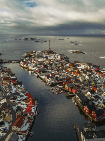 Aerial view of quaint red roofed buildings nestled amidst the icy waters and rocky isles under a moody sky Henningsv&aelig;r Nordland Norway.