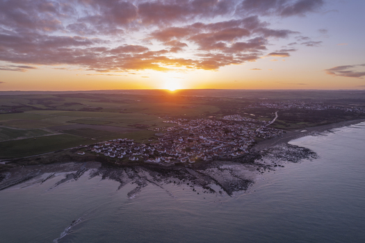 Aerial view of the coastal village of Audresselles at sunset with traditional houses rocky shoreline and calm sea under a vibrant sky in Audresselles Hauts de France France.