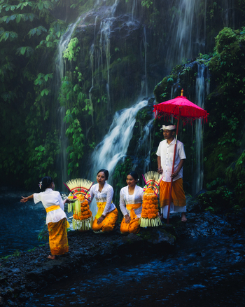 Bali Indonesia View of Balinese people in traditional attire their saffron and white robes contrasting against the cool dark tones of the cascading waterfall and lush foliage. Bali Indonesia View of Balinese people in traditional attire their saffron and white robes contrasting against the cool dark tones of the cascading waterfall and lush foliage.