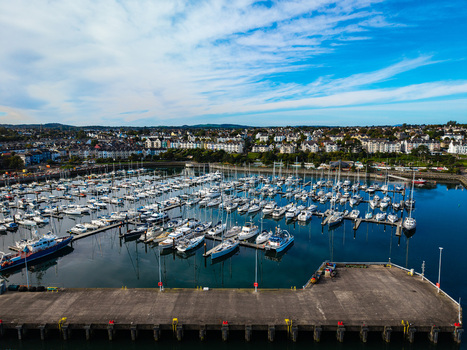 Aerial view of Bangor Harbour and Town with sailboats moored in the marina surrounded by coastal buildings under a blue sky in Bangor Northern Ireland United Kingdom.