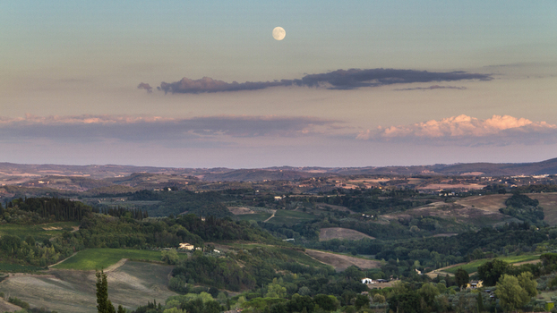 View of rolling green hills bathed in the soft glow of twilight with a full moon hanging above casting shadows across the landscape San Gimignano Tuscany Italy. View of rolling green hills bathed in the soft glow of twilight with a full moon hanging above casting shadows across the landscape San Gimignano Tuscany Italy.
