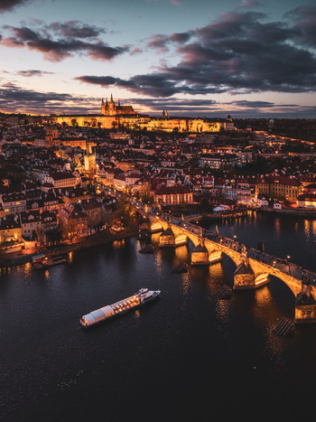Aerial view of Prague Castle and Charles Bridge illuminated at dusk with a boat on the Vltava river in Prague Prague Czechia. Aerial view of Prague Castle and Charles Bridge illuminated at dusk with a boat on the Vltava river in Prague Prague Czechia.