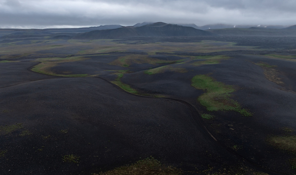 Aerial view of volcanic landscape with black lava fields and patches of green moss under a cloudy sky in Iceland. Aerial view of volcanic landscape with black lava fields and patches of green moss under a cloudy sky in Iceland.