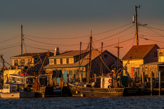 View of Martha s Vineyard with fishing boats docked at the harbor beside shingled buildings under a golden sunset sky in Edgartown Massachusetts United States.