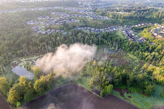 Aerial view of a misty landscape featuring a small pond dense green forests and a plowed agricultural field near a residential neighborhood Alderton Washington United States. Aerial view of a misty landscape featuring a small pond dense green forests and a plowed agricultural field near a residential neighborhood Alderton Washington United States.