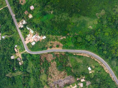 Aerial view of a winding asphalt road cutting through lush green tropical vegetation and scattered rural houses in Ghana. Aerial view of a winding asphalt road cutting through lush green tropical vegetation and scattered rural houses in Ghana.