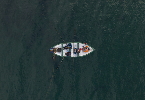Aerial view of a small rowing boat with four people on the deep dark waters of Hardangerfjord in Blurnes Vestland Norway. Aerial view of a small rowing boat with four people on the deep dark waters of Hardangerfjord in Blurnes Vestland Norway.