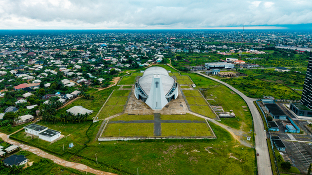 Aerial view of a modern church with a cross on its facade surrounded by green lawns and the urban landscape of the city in Uyo Akwa Ibom Nigeria. Aerial view of a modern church with a cross on its facade surrounded by green lawns and the urban landscape of the city in Uyo Akwa Ibom Nigeria.