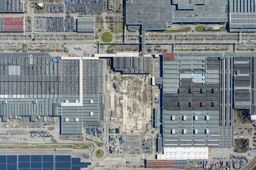 Aerial view of sprawling industrial buildings and parking lots create a textured tapestry of concrete and steel reflecting the pale sunlight Sausheim Grand Est France.