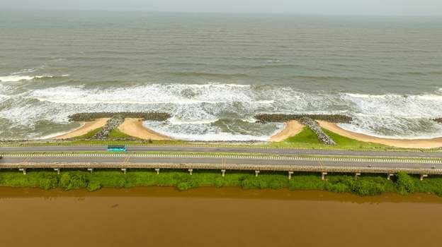 Aerial view of Maravanthe beach with a road running between the Arabian Sea and the Souparnika River featuring crashing waves and lush green vegetation in Maravanthe Karnataka India. Aerial view of Maravanthe beach with a road running between the Arabian Sea and the Souparnika River featuring crashing waves and lush green vegetation in Maravanthe Karnataka India.