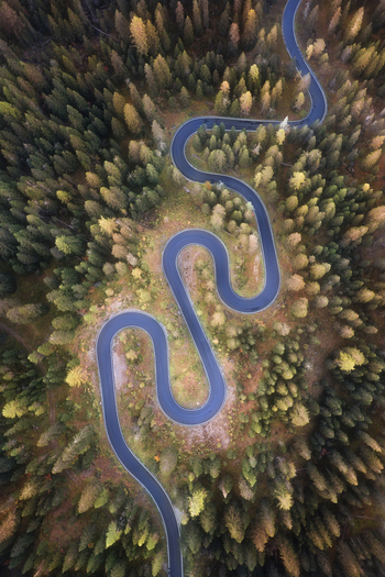 Aerial view of the winding Passo Giau mountain road snaking through a dense forest of autumn larches in Colle Santa Lucia Veneto Italy. Aerial view of the winding Passo Giau mountain road snaking through a dense forest of autumn larches in Colle Santa Lucia Veneto Italy.