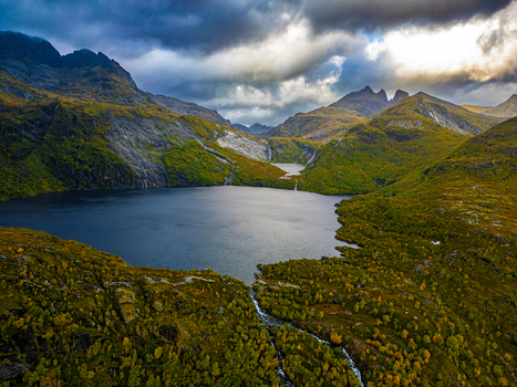 Aerial view of Stuvdalsvatnet lake surrounded by rugged mountains lush green and yellow autumn vegetation and dramatic cloudy sky in Moskenes Nordland Norway. Aerial view of Stuvdalsvatnet lake surrounded by rugged mountains lush green and yellow autumn vegetation and dramatic cloudy sky in Moskenes Nordland Norway.