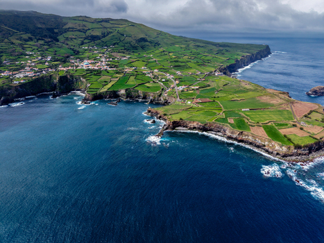 Aerial view of verdant fields meet the rugged coastline as waves crash against cliffs near Estrada do Farol Flores A&ccedil;ores Portugal.
