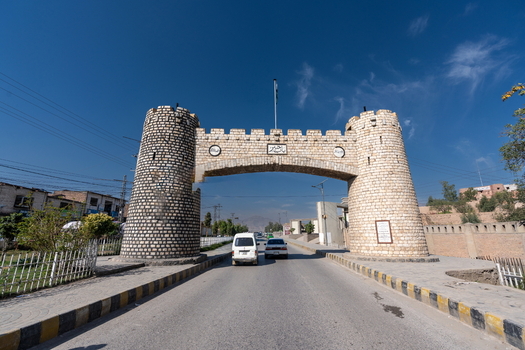 View of the historic Khyber Pass stone archway spanning a road with cars passing underneath under a clear blue sky in Khyber District Khyber Pakhtunkhwa Pakistan.