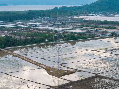 Aerial view of a high voltage transmission tower in flooded fields with a major transmission substation and solar panel farm in the background in Central Seberang Perai Penang Malaysia. Aerial view of a high voltage transmission tower in flooded fields with a major transmission substation and solar panel farm in the background in Central Seberang Perai Penang Malaysia.