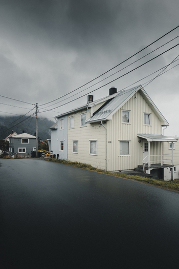 View of a traditional wooden house in the village of Henningsvaer under a moody overcast sky with power lines and a wet asphalt road in the foreground Henningsvaer Nordland Norway. View of a traditional wooden house in the village of Henningsvaer under a moody overcast sky with power lines and a wet asphalt road in the foreground Henningsvaer Nordland Norway.