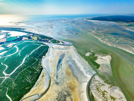 Aerial view of the Baie de Somme featuring winding tidal channels expansive salt marshes and intricate sand patterns along the coast in Saint Valery sur Somme Hauts de France France. Aerial view of the Baie de Somme featuring winding tidal channels expansive salt marshes and intricate sand patterns along the coast in Saint Valery sur Somme Hauts de France France.
