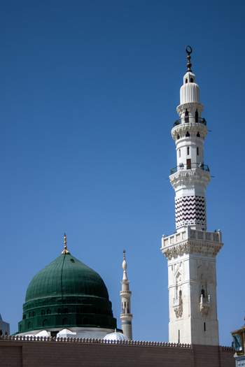 View of the green dome and minaret of Al Masjid e Nabawi under a clear blue sky in Madinah Al Madinah Province Saudi Arabia.