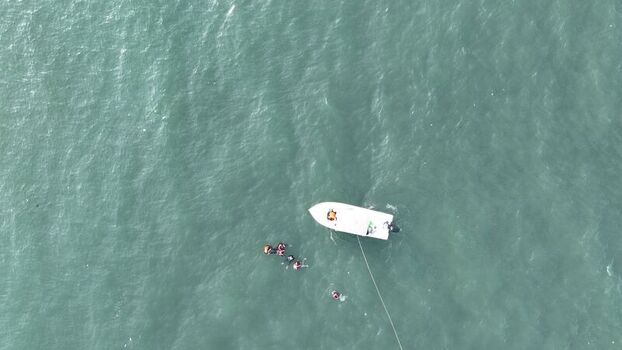 Aerial view of a small white boat with people swimming in the turquoise sea near Pulau Lima Resort in Kasemen Banten Indonesia. Aerial view of a small white boat with people swimming in the turquoise sea near Pulau Lima Resort in Kasemen Banten Indonesia.