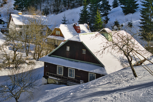 View of snow blanketed cottages with dark wood facades nestled among frosted trees in a serene winter landscape Moce Banska Bystrica Region Slovakia.