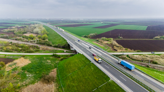 Aerial view of a highway cutting through a vibrant tapestry of green fields and dark earth framed by an overcast sky Sremska Mitrovica Vojvodina Serbia. Aerial view of a highway cutting through a vibrant tapestry of green fields and dark earth framed by an overcast sky Sremska Mitrovica Vojvodina Serbia.