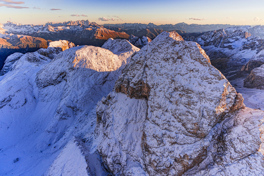 Aerial view of snow dusted peaks glow with the warm hues of the rising sun casting long shadows across the majestic landscape Catinaccio range Trentino South Tyrol Italy.