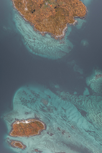 Aerial view of rocky islands with autumn vegetation surrounded by turquoise waters and shallow sea beds Senja Troms Norway.